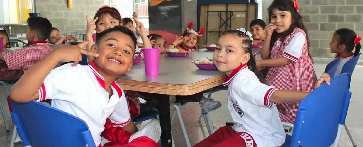 Foto de niños sonriendo en el restaurante de una escuela con su refrigerio escolar